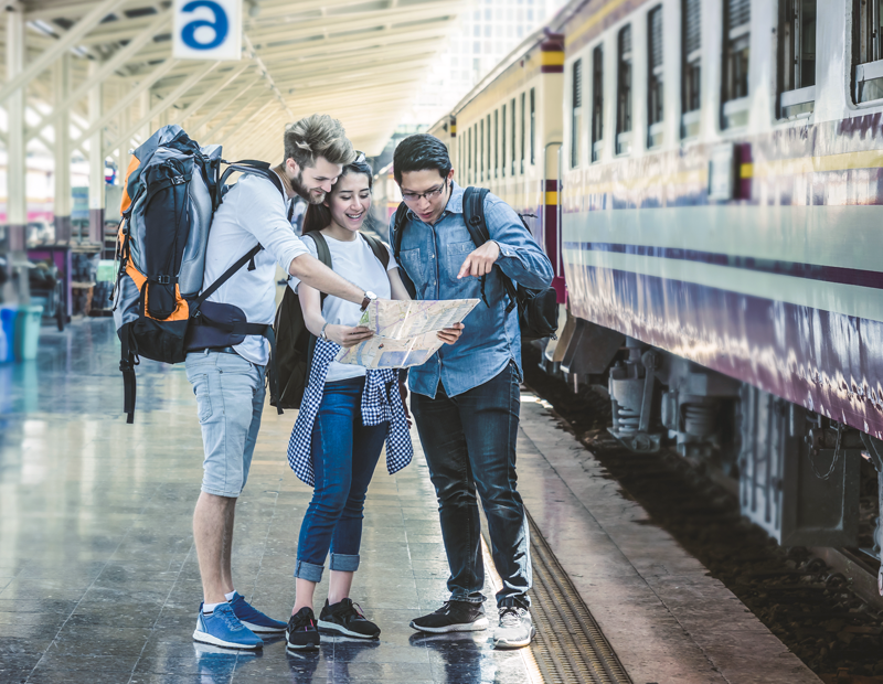 Travelers with backpacks checking a map at a train station in Thailand before boarding a long-distance train
